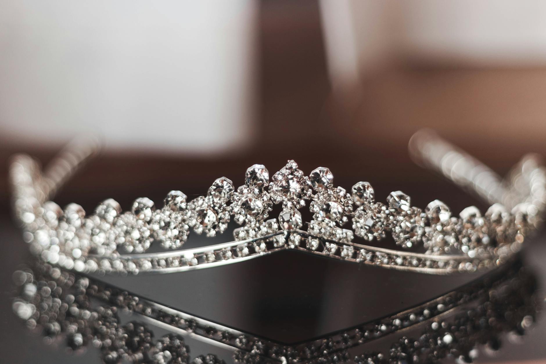 Close-up of a sparkling diamond tiara placed on a reflective surface. Perfect for wedding or gala events.