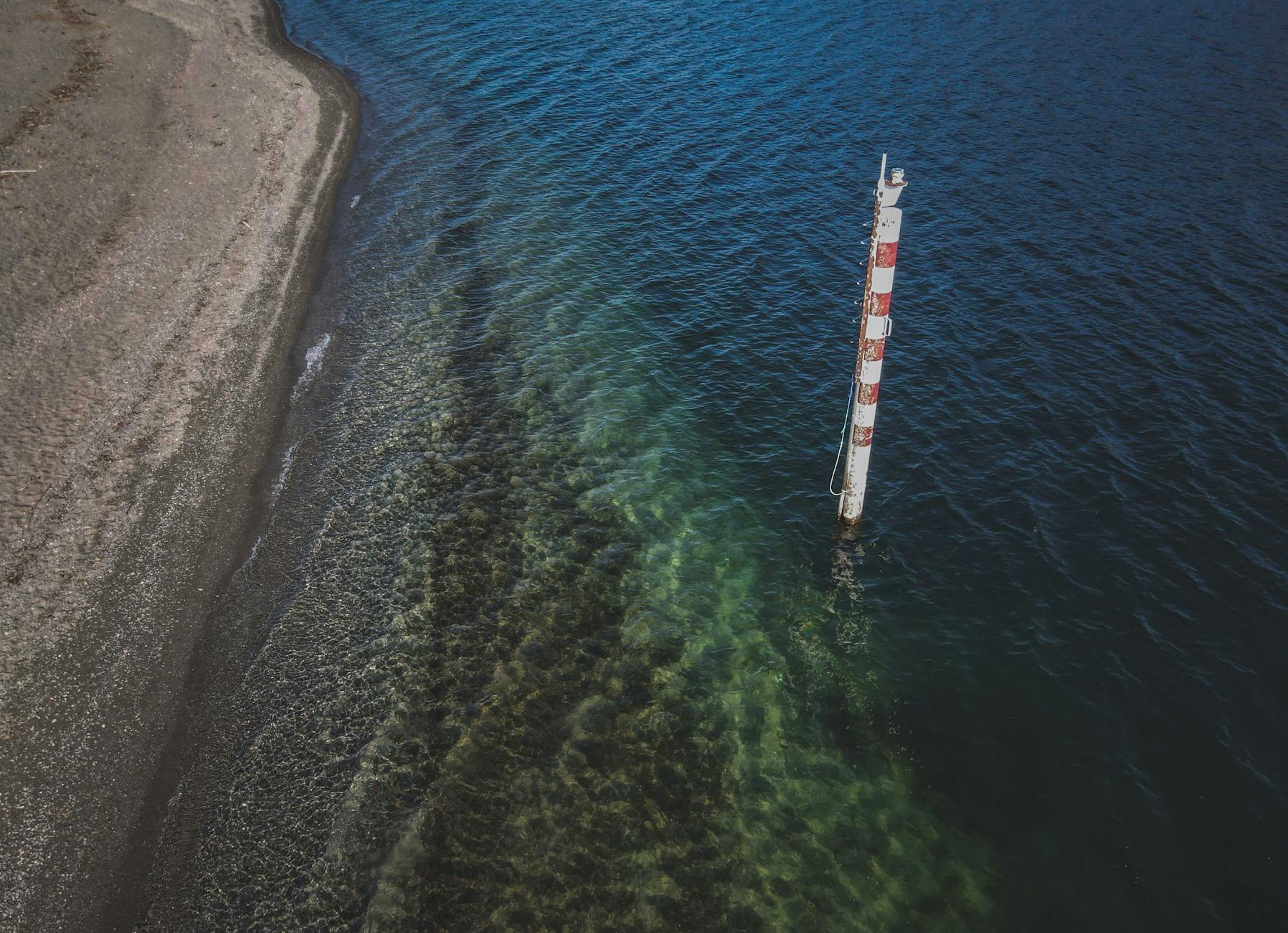 Aerial view of a beach with a coastal tower and clear blue sea.