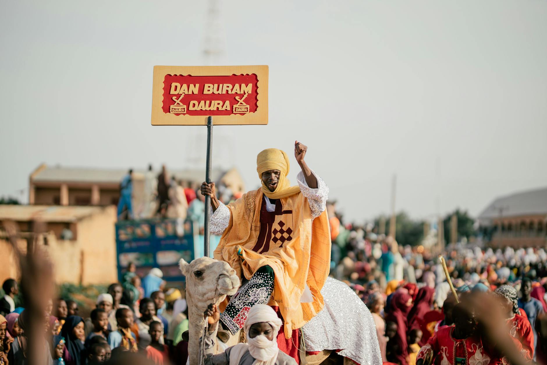 Man in traditional attire on camel at Nigerian cultural festival with crowd.