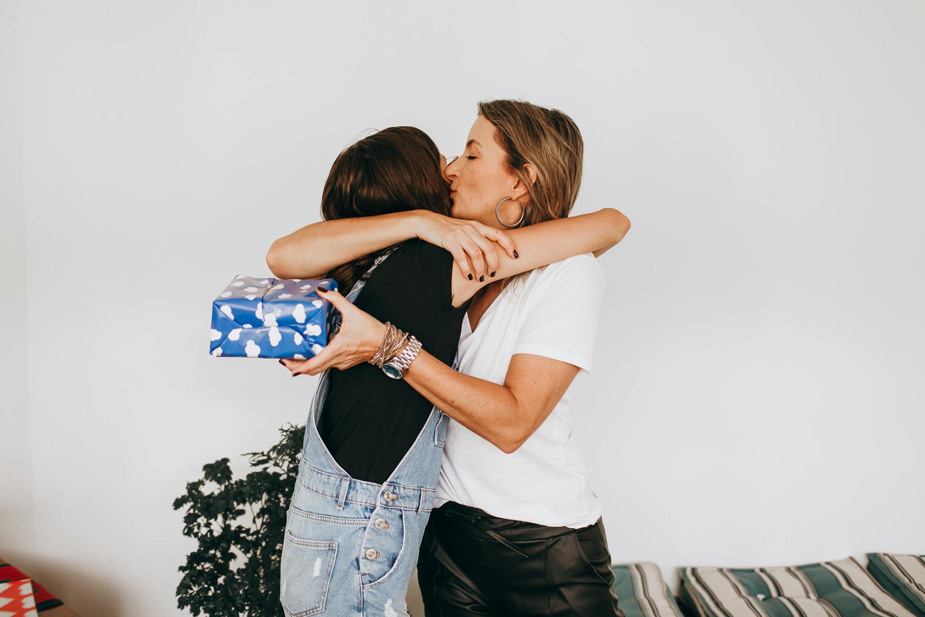 A touching moment of a mother and daughter embracing with a gift in hand indoors.