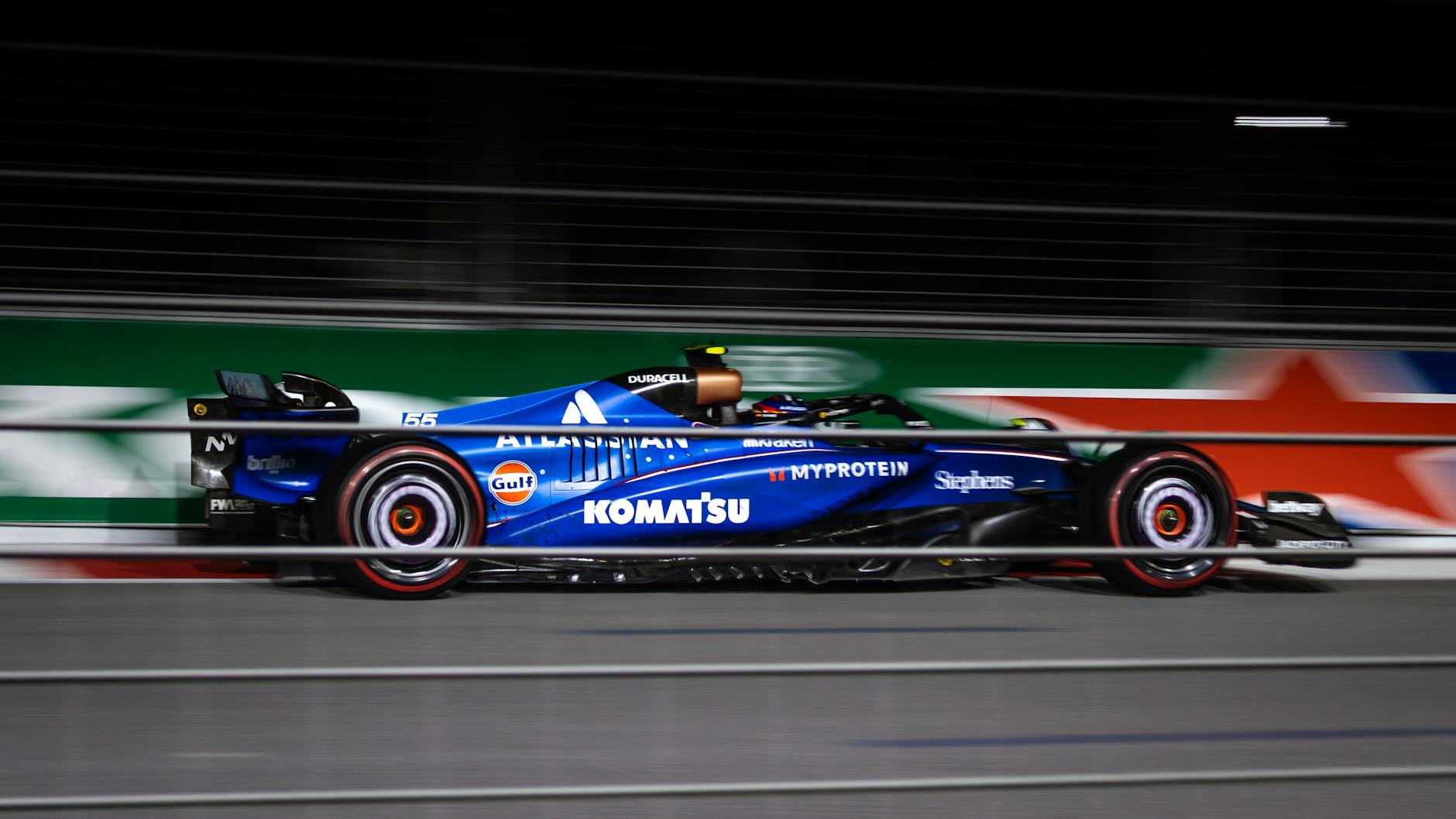 Blue Formula car speeding on track during night race.