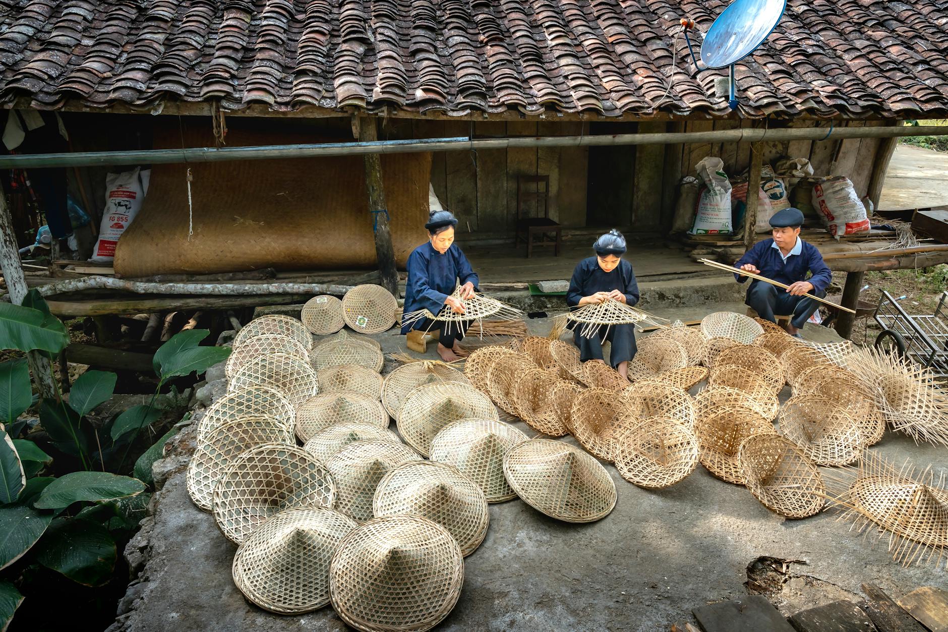 Three artisans crafting wicker baskets in a rural setting, showcasing traditional craftsmanship.