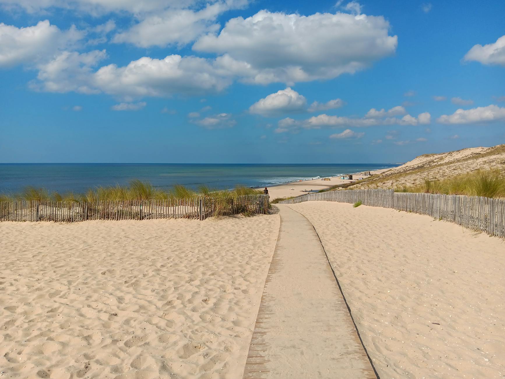Beautiful pathway leading to a serene beach at Montalivet, under a vibrant blue sky.