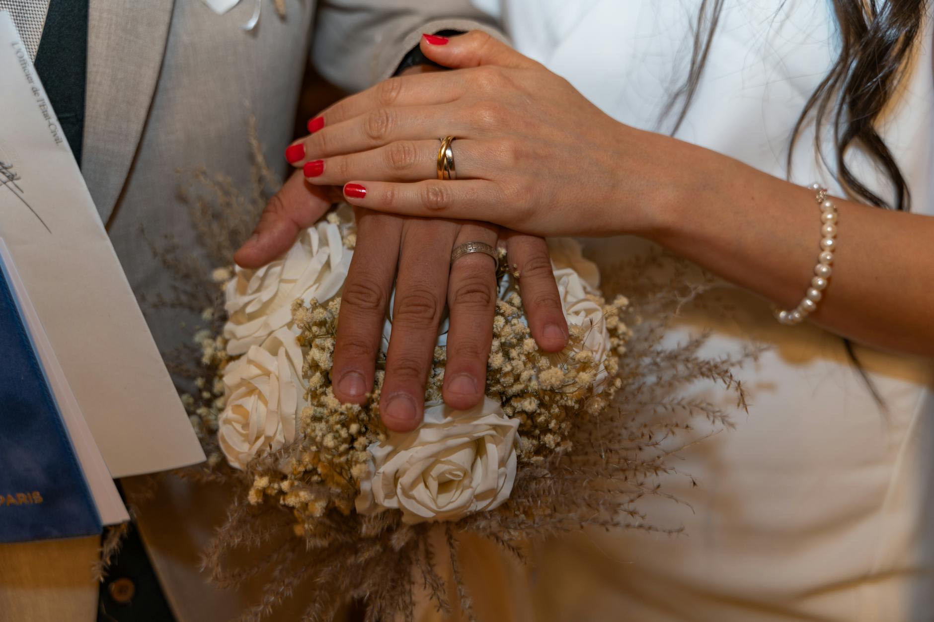 Close-up of bride and groom's hands with wedding rings over floral bouquet, symbolizing love and unity.