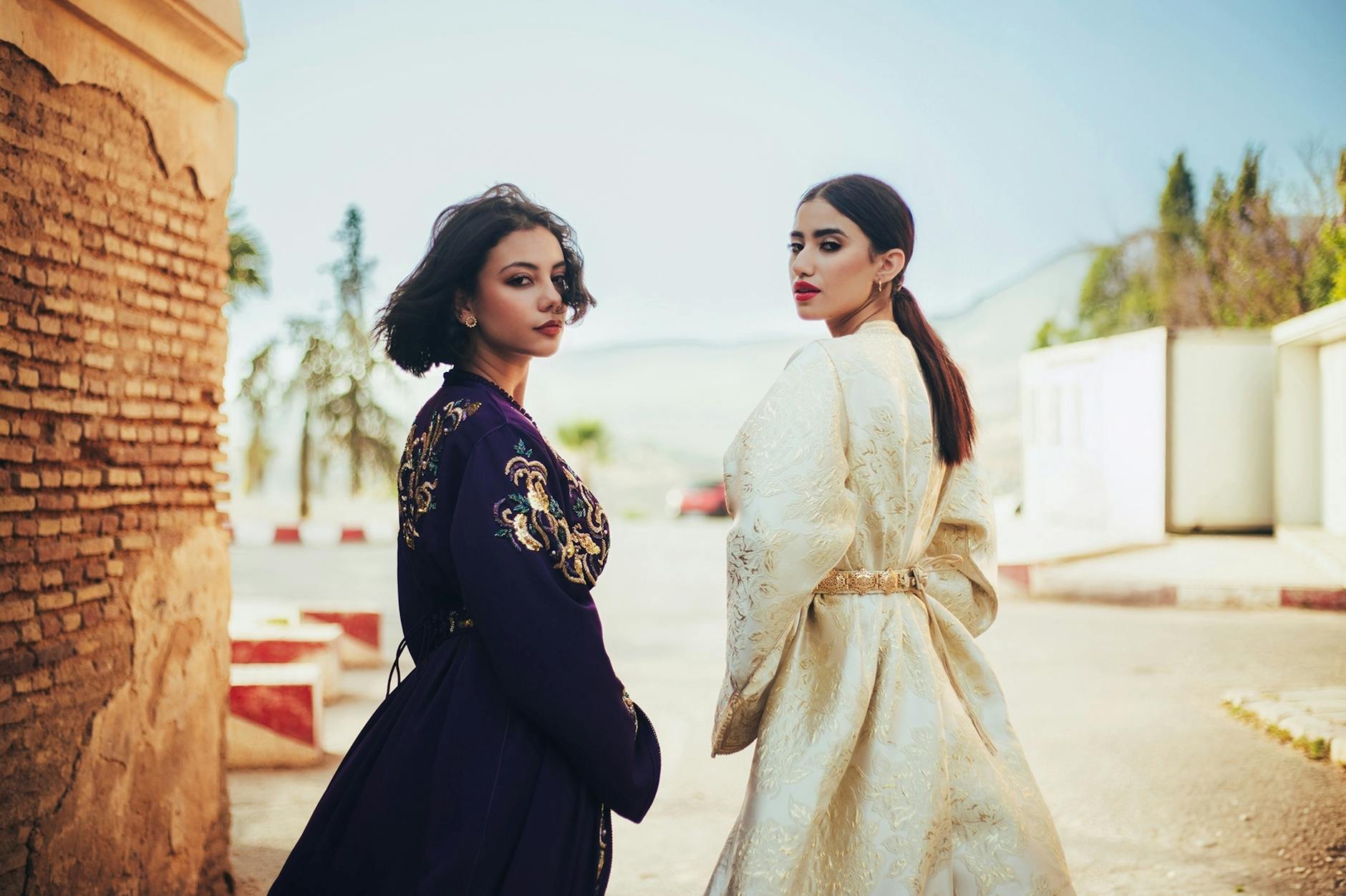 Two women outdoors in elegant traditional clothing with intricate embroidery and vibrant patterns.