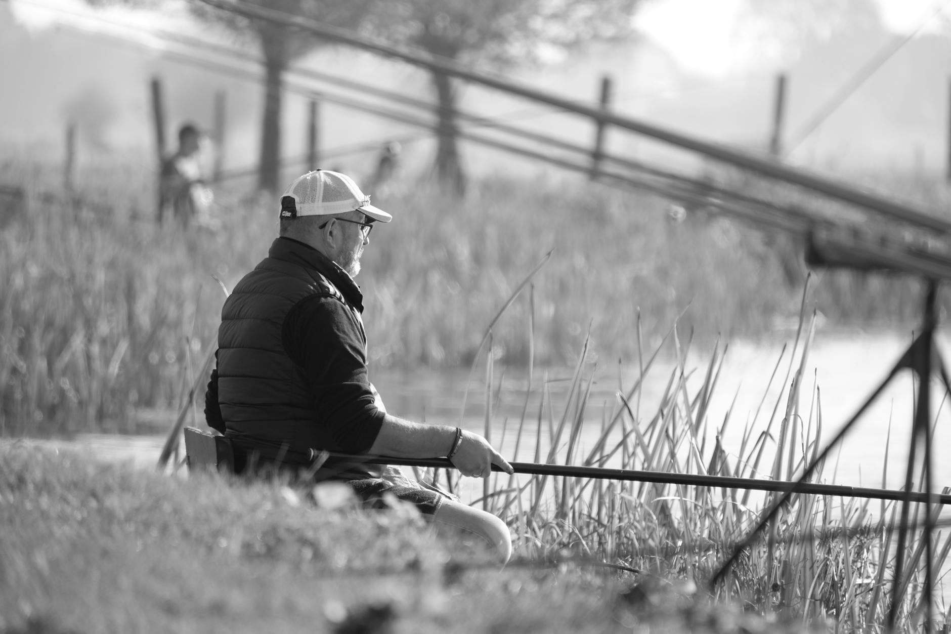 A serene black and white scene of an adult man fishing by the lake, enjoying a tranquil morning.