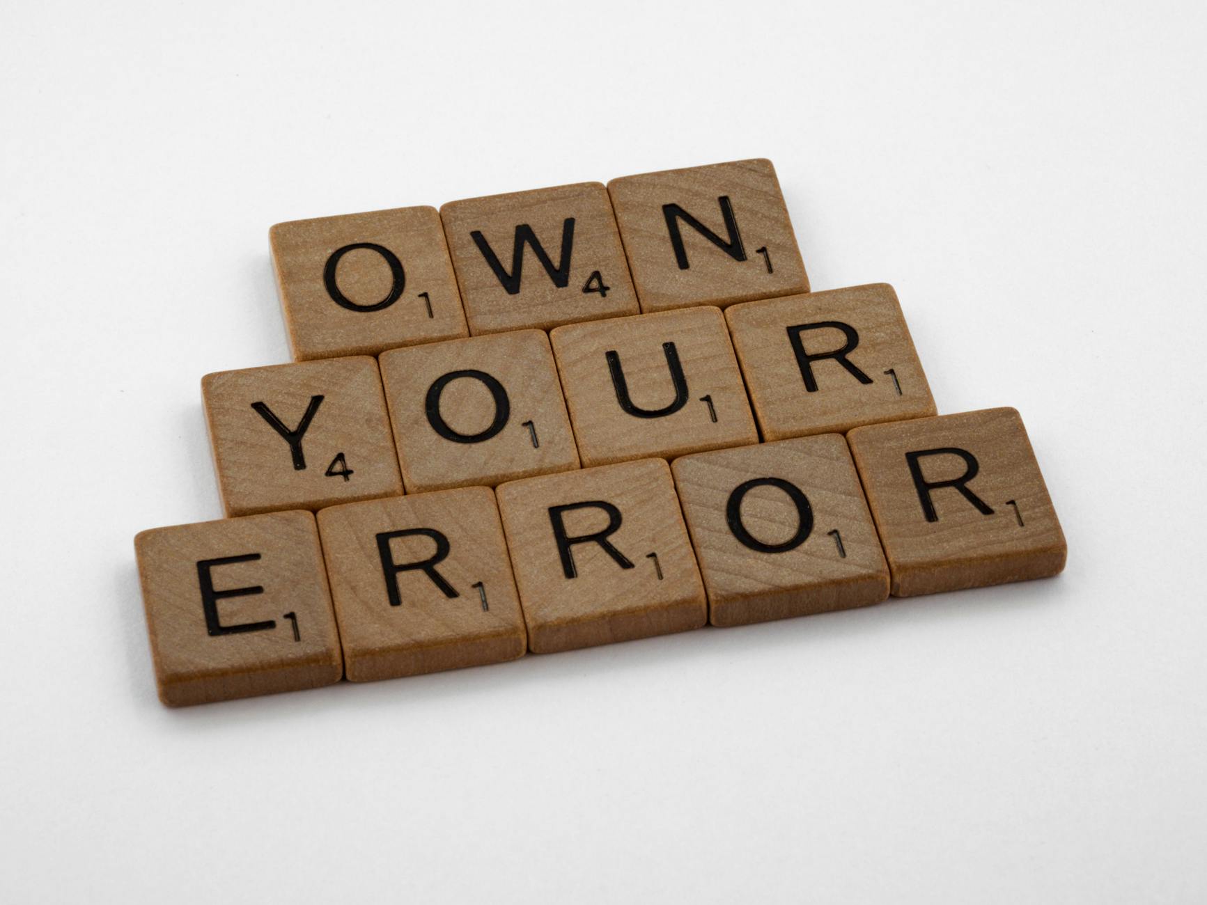 Scrabble tiles forming the phrase 'OWN YOUR ERROR'. Great for concepts of accountability and motivation.